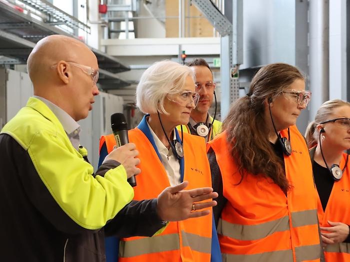 en man och två kvinnor med varselkläder i fabrik, tittar intresserat mot objekt utanför bild