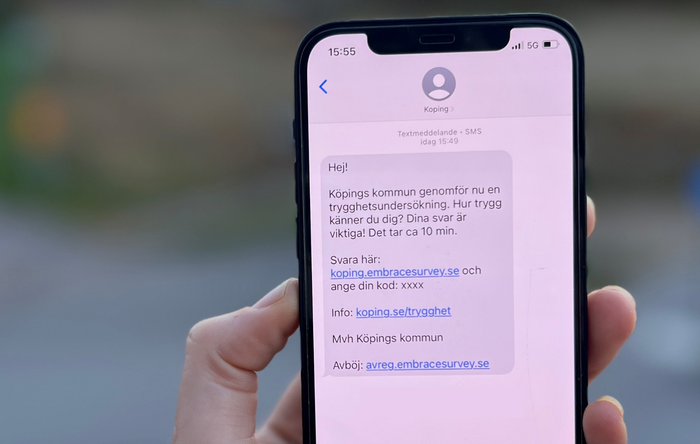 Bild på telefon med SMS: Köpings kommun genomför nu en trygghetsundersökning. Hur trygg känner du dig? Dina svar är viktiga! Det tar ca 10 min.Svara här: koping.embracesurvey.se och ange din kod: xxxxInfo: koping.se/trygghetMvh Köpings kommunAvböj: avreg.embracesurvey.se