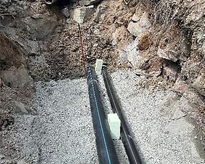 Två ledningar ligger i grusad schakt mellan bergväggar.