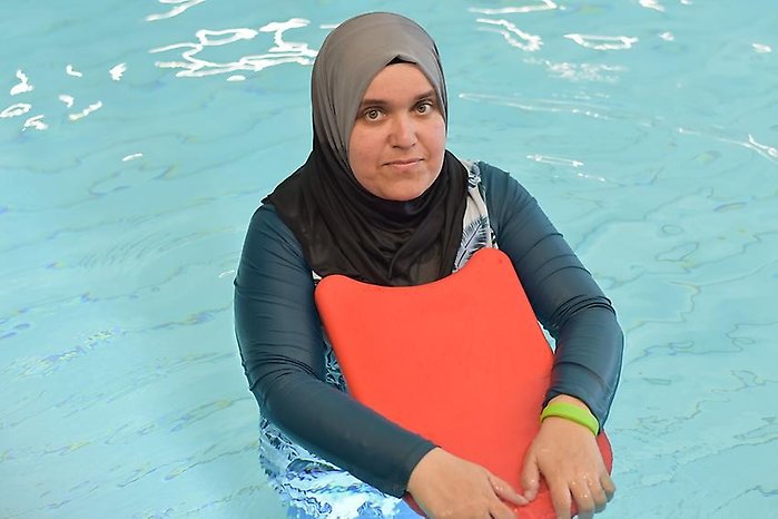 Kvinna står i en pool och håller en flytplatta mot kroppen.